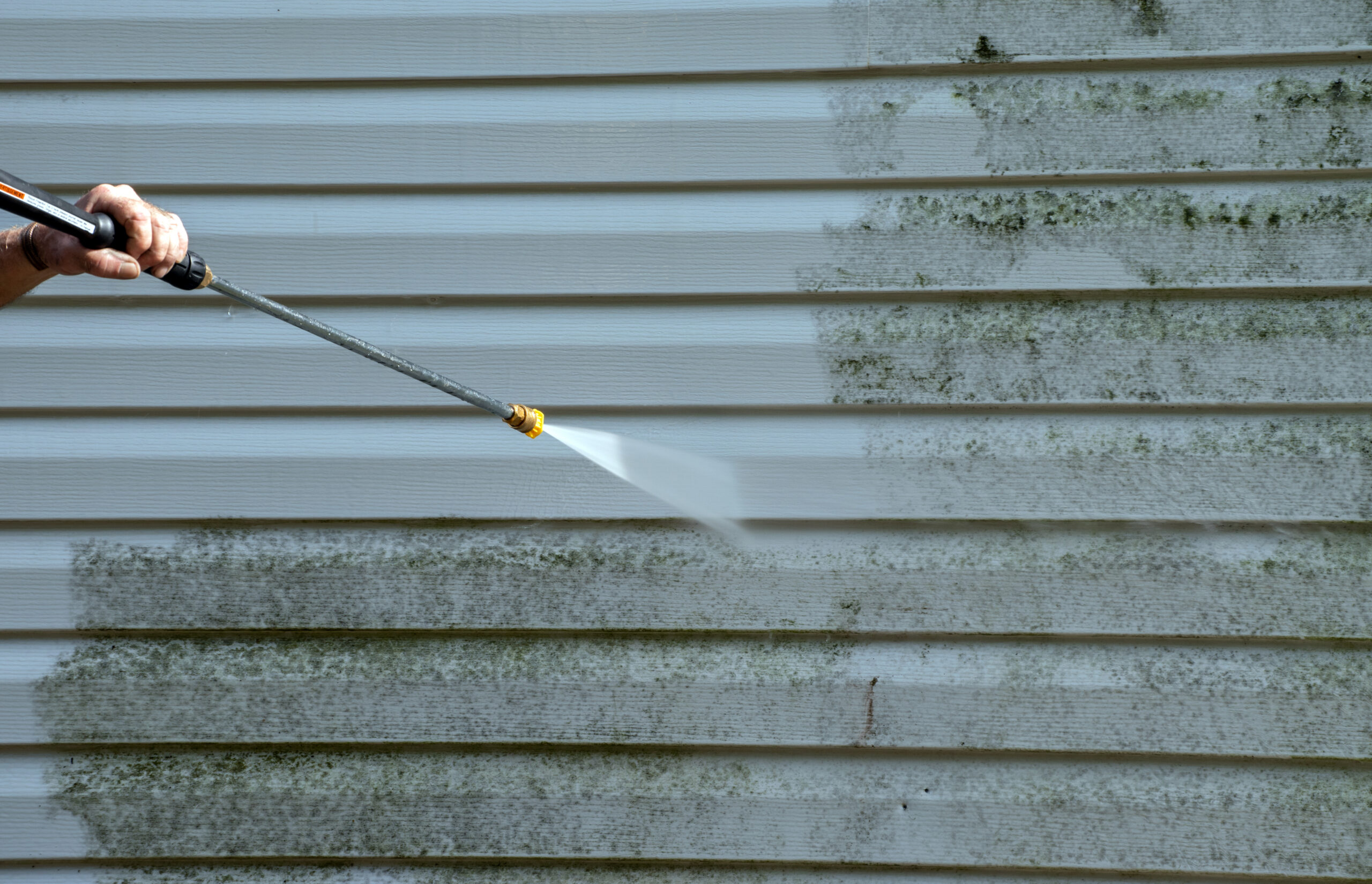 An A&A Window Cleaning employee using a power washer to clean mold from vinyl siding